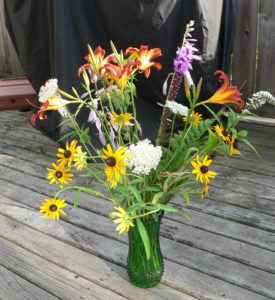 A vase with lillies and brown eyed susans on a wood porch